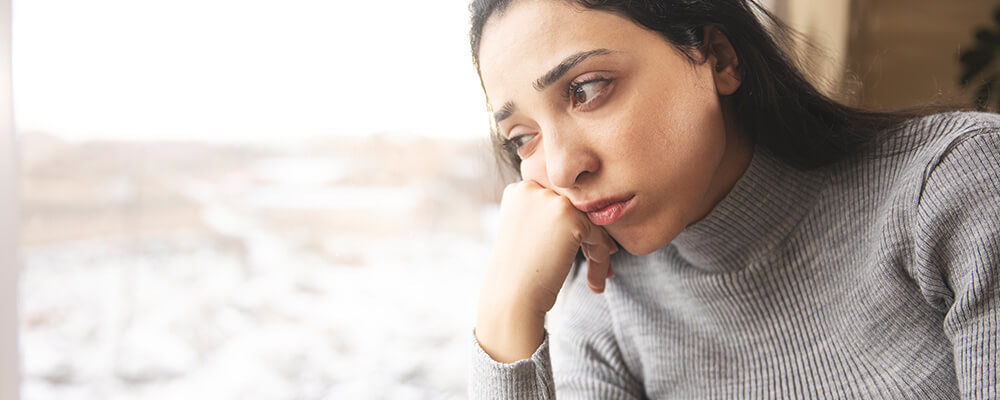 Mujer mirando por una ventana con expresión preocupada 