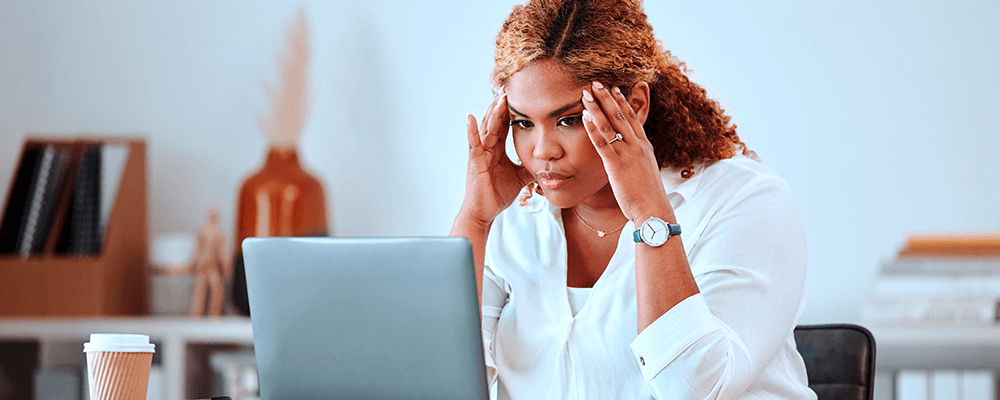 Mujer frente a una computadora tocándose las sienes por estrés